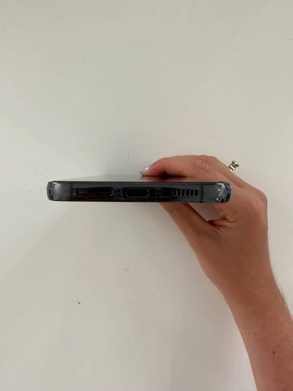 Nahaufnahme der Anschlüsse eines getesteten Samsung-Smartphones von einer Hand vor eine helle Wand gehalten.