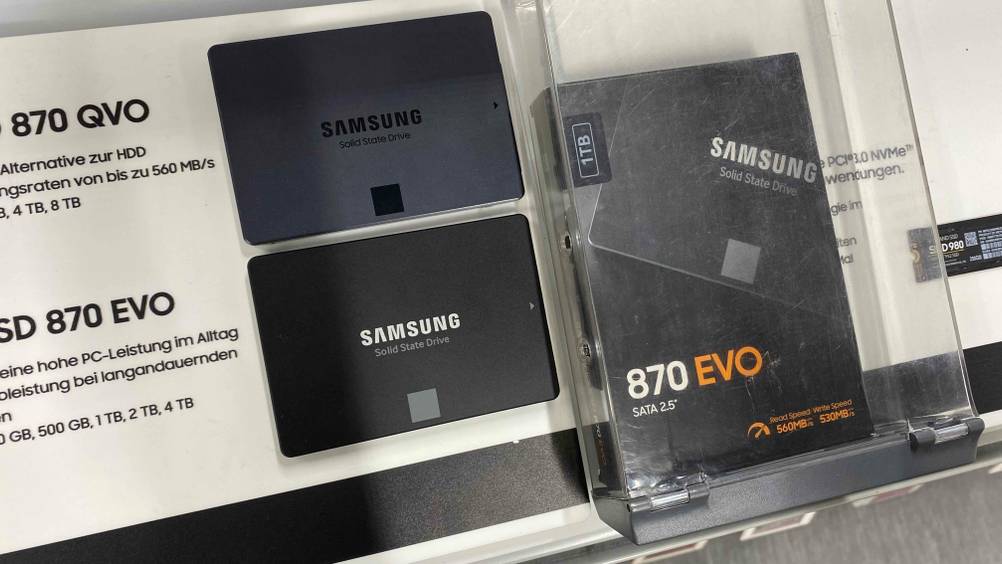 Samsung-SSD getestet: Eine SSD auf einer Infotafel, daneben eine Originalverpackung in einer transparenten Box.