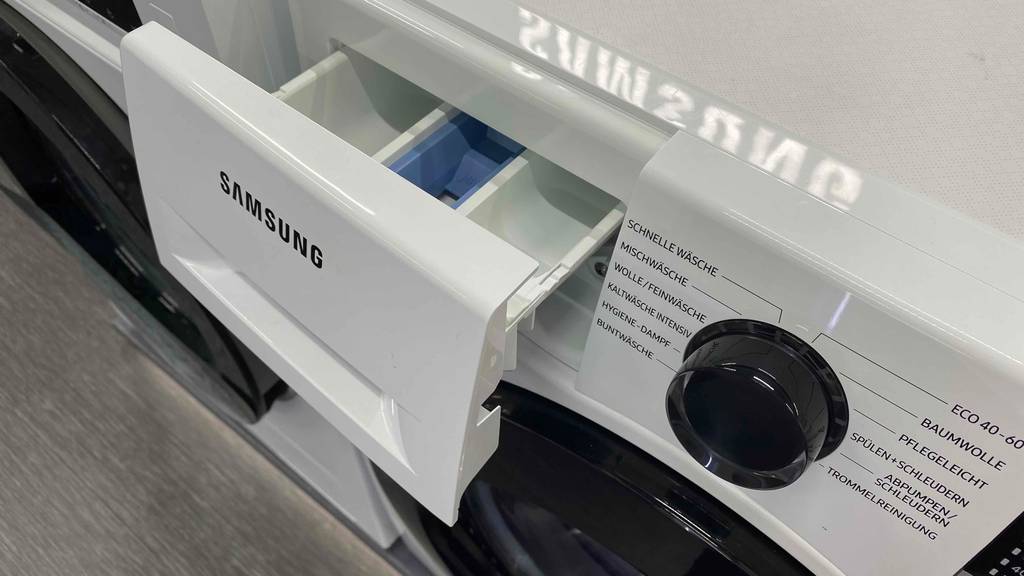 Im Test: geöffnetes Waschmittelfach und Programmdrehknopf einer Samsung Waschmaschine.