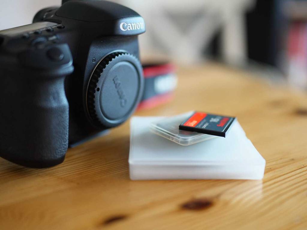 CF-Karten im Test: eine SanDisk Karte, liegt auf ihrem Kunststoffbehälter auf einem Holztisch neben einer Canon-Digitalkamera.