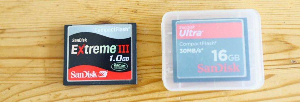 Zwei getestete CF-Karten befinden sich nebeneinander auf einer Holzfläche, ein Extreme 3 mit 1.0 GB und eine Ultra mit 16 GB Speicherplatz.