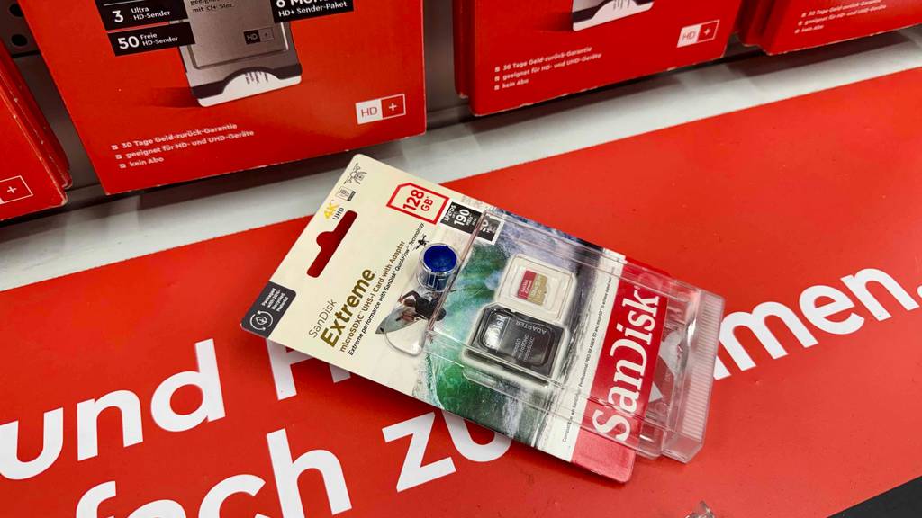 Im Test: Eine Micro SD-128 GB Karte der Marke SanDisk liegt original verpackt auf einem roten Plakat inklusive Schriftzug.