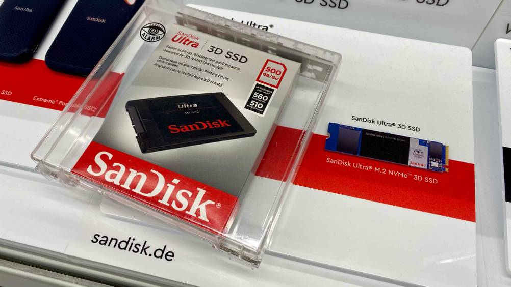 SSD (500GB) getestet: Eine SSD auf einer Infotafel befestigt, daneben die Originalverpackung in einer transparenten Box.