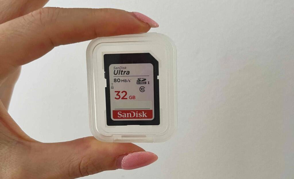 Vor einer vor weißen Wand halten Damenfinger die transparente Aufbewahrungsbox inklusive einer 32-GB-SD-Karte im Test.