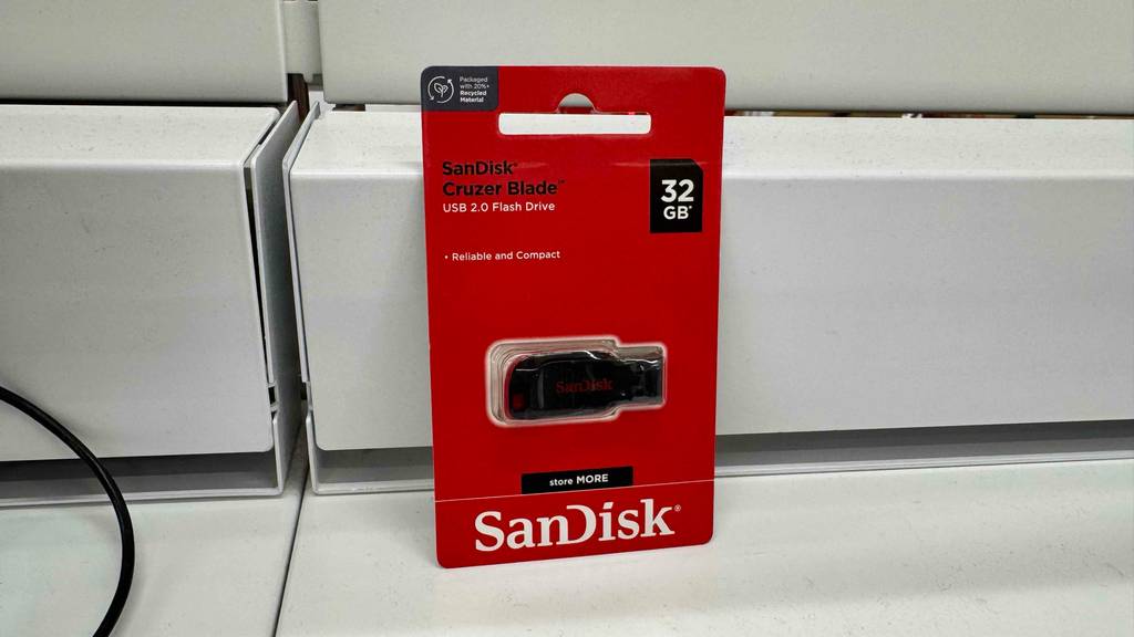 Ein USB-Stick mit 32 GB Speicherplatz im Test lehnt innerhalb seiner roten Originalverpackung an einer weißen Wand.