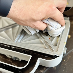 Eine Person wischt den getesteten Breville-Sandwichmaker mit einem Tuch ab.