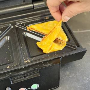 Sandwichmaker-Test: Eine Person entfernt geschmolzenen Käse aus dem Krups-Sandwichmaker.