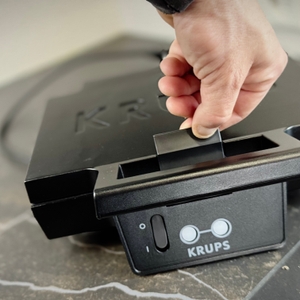 Eine Person öffnet den Verschluss des getesteten Sandwichmakers von Krups.