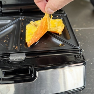 Eine Person entfernt geschmolzenen Käse aus dem getesteten Sandwichmaker von Tefal.