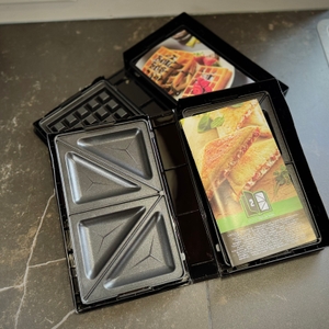 Sandwichmaker im Test: In zwei Aufbewahrungsboxen liegen jeweils eine Sandwich-Platte sowie eine Waffel-Platte vom Tefal-Sandwichmaker.