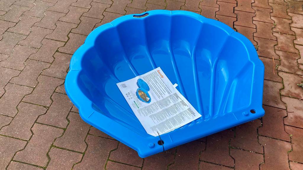 Ein Sandkasten aus Plastik steht zum testen auf einem Pflastersteinboden.