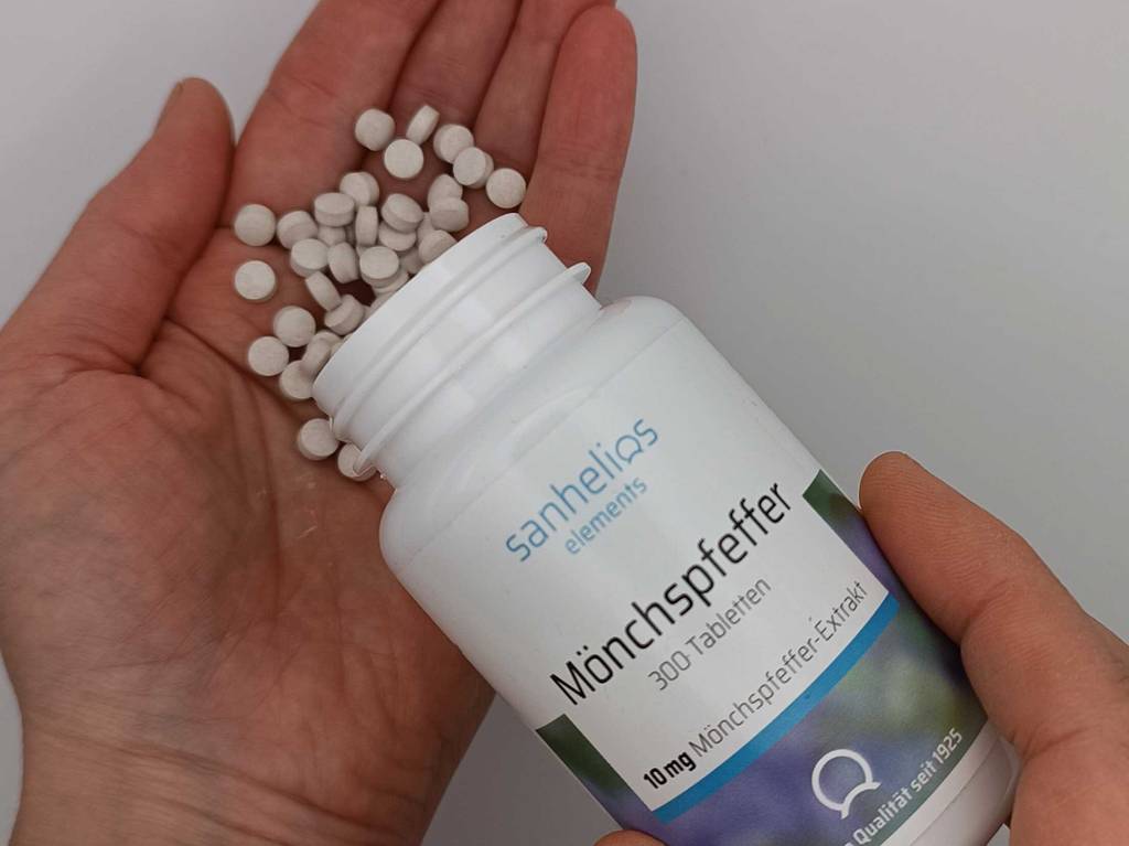 Getesteter Mönchspfeffer in Tabletten liegt auf einer Hand, während eine andere Hand die Dose mit 300 Tabletten festhält.