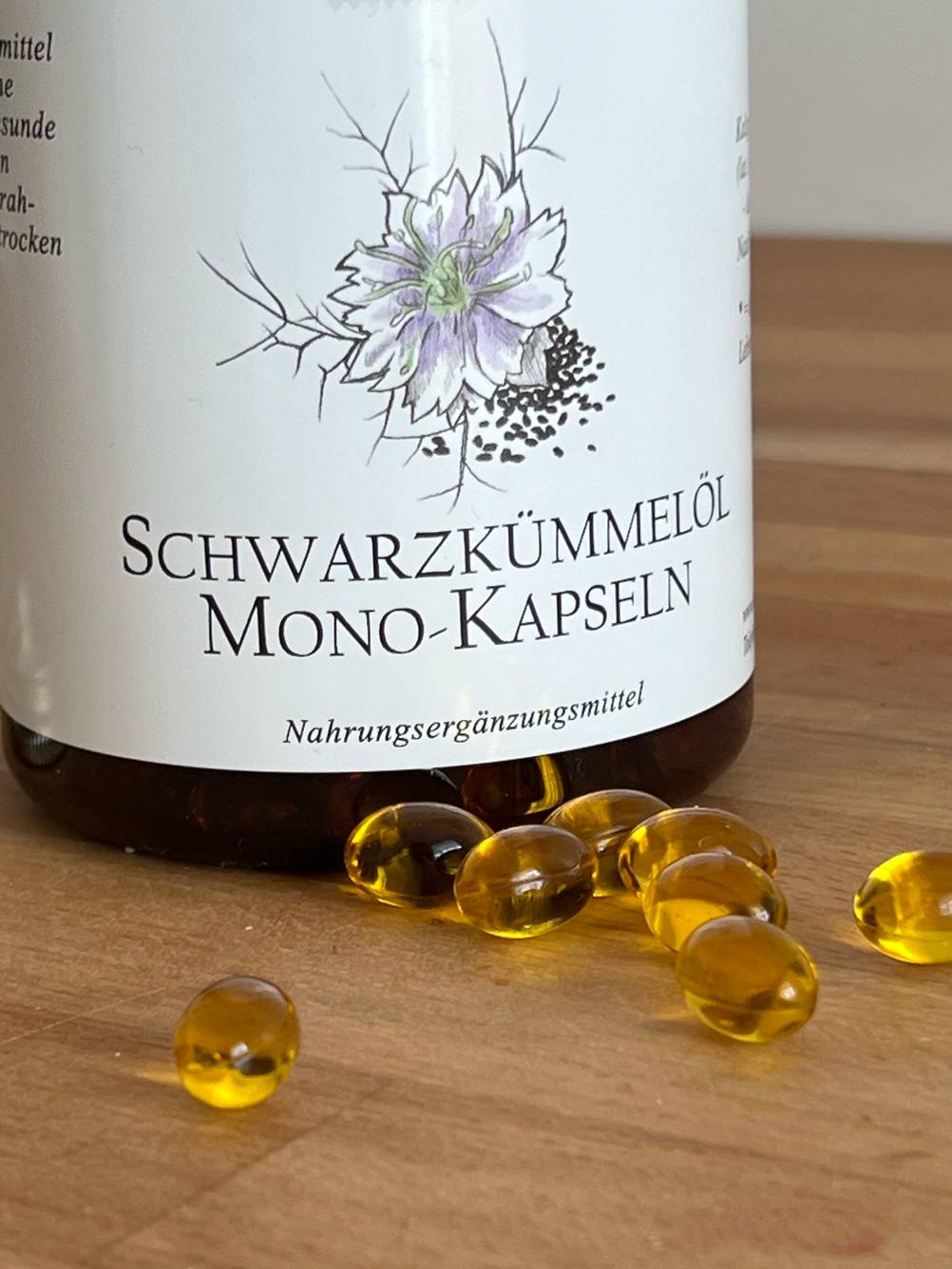 Im Test: Nahaufnahme des Logos einer Dose Schwarzkümmelöl-Kapseln, davor liegen einige Kapseln verstreut.