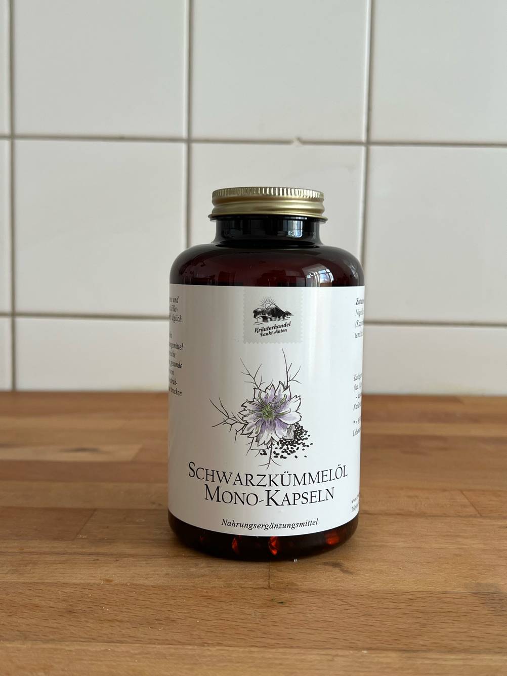 Eine Dose Schwarzkümmelöl-Kapseln im Test von vorne auf einer Holzfläche vor einer weißen Fließenwand.