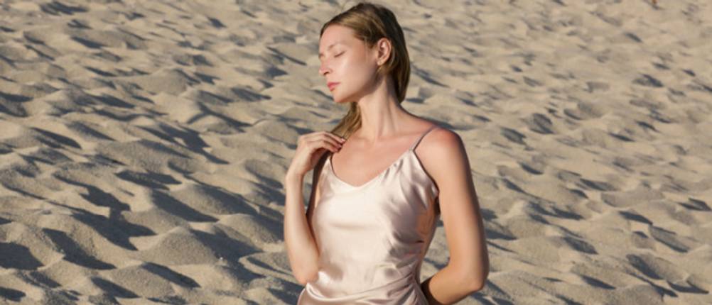 Satin-Kleid im Test: junge Frau mit sandfarbenem Satin-Kleid am Strand.