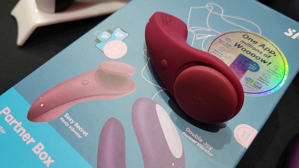 Paarvibrator getestet: ein penisförmiger, roter Vibrator inklusive Einschaltknopf aus der Partner Box von Satisfyer liegt auf der Beschreibung.
