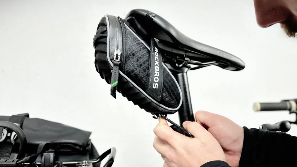 Eine Person befestigt die Rockbros C16-BK Satteltasche am Fahrradsattel. Die Klettverschlüsse werden festgezogen, um die Tasche sicher zu fixieren.