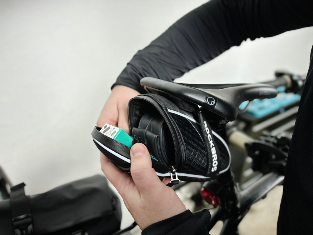 Ein Radfahrer öffnet die Rockbros C16-BK Satteltasche und verstaut einen Ersatzschlauch und weiteres Zubehör. Die Tasche ist teilweise befüllt.