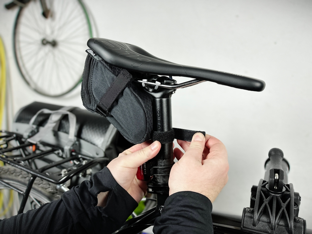 Eine Person befestigt die Vaude Race Light Satteltasche am Fahrradsattel. Die Klettverschlüsse werden für eine sichere Fixierung um die Sattelstütze gelegt.