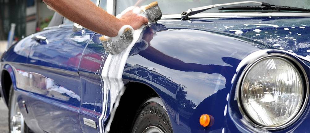 Ein Mann wäscht mit einem Schwamm einen blauen Oldtimer.