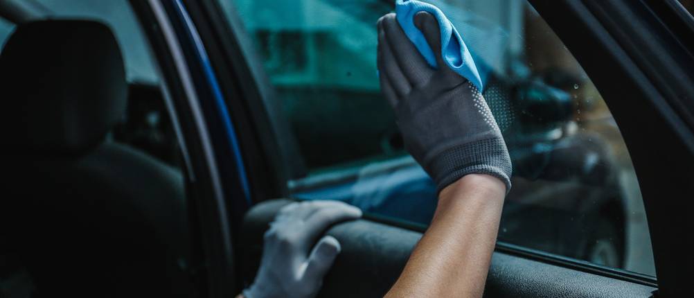 Ein Mann trägt zwei Putzhandschuhe und putzt die Innenscheiben eines Autos.