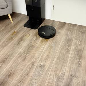 Der Saug-Wisch-Robotoer steht neben seiner Station auf einem Laminatboden.