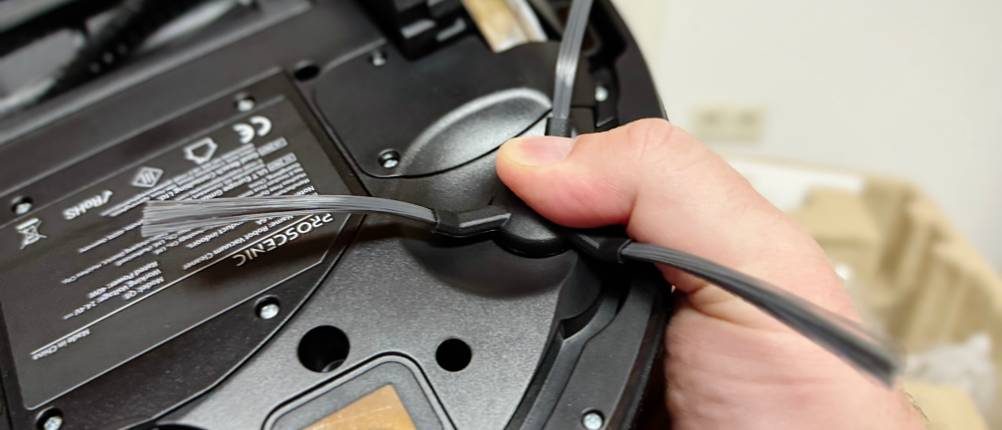 Eine Hand hält den Saug-Wisch-Roboter umgedreht, sodass die Bürsten nach oben zeigen.