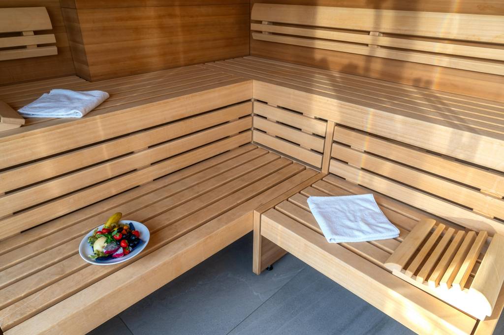 Sauna-Kopfstütze im Test: Eine Sauna mit Bänken über Eck, Handtüchern und einem Obstteller nebst einer organisch geformten Stütze.