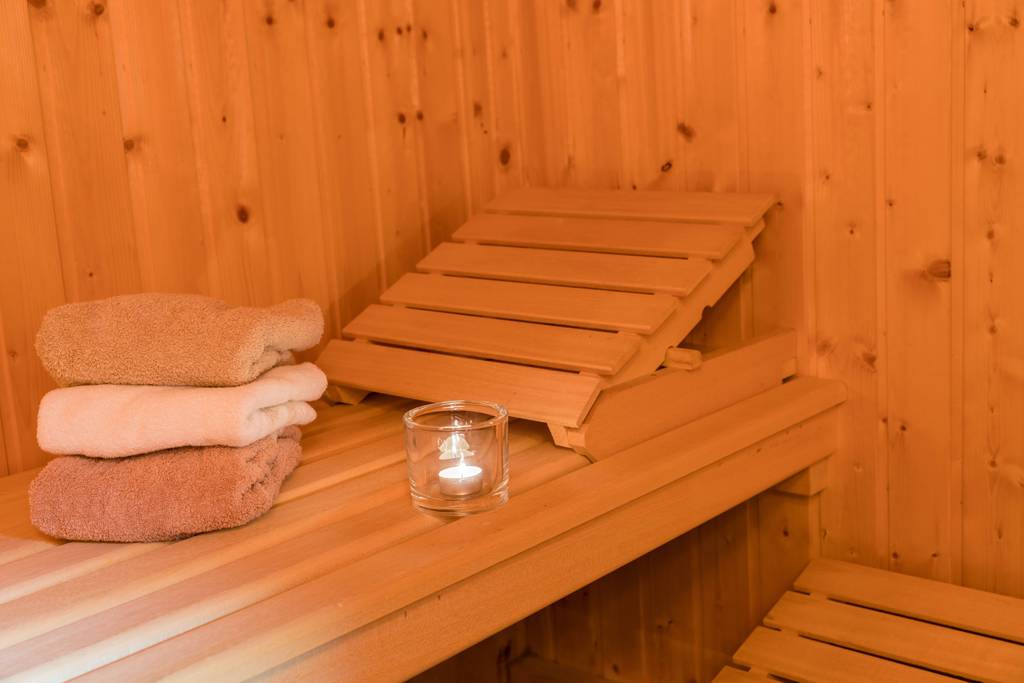 Sauna-Kopfstütze im Test: Eine verstellbare Holzstütze in einer Sauna mit drei gefalteten Handtüchern und einem Teelicht in einem Glasbehälter