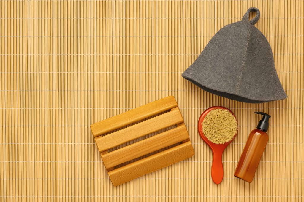 Sauna-Kopfstütze im Test: sehr kleine Kopfstütze, Filzhut und Kosmetikprodukte auf einer Matte aus Bambus