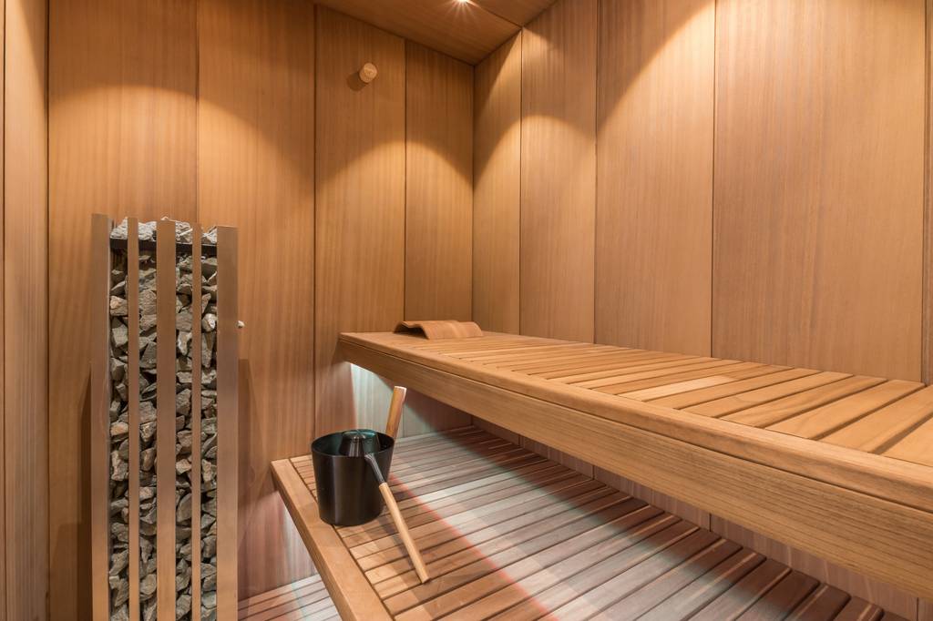 Sauna-Kopfstütze im Test: Sauna mit Holzwänden, zwei breiten Bänken, Badezubehör und Heizelement mit Steinen.