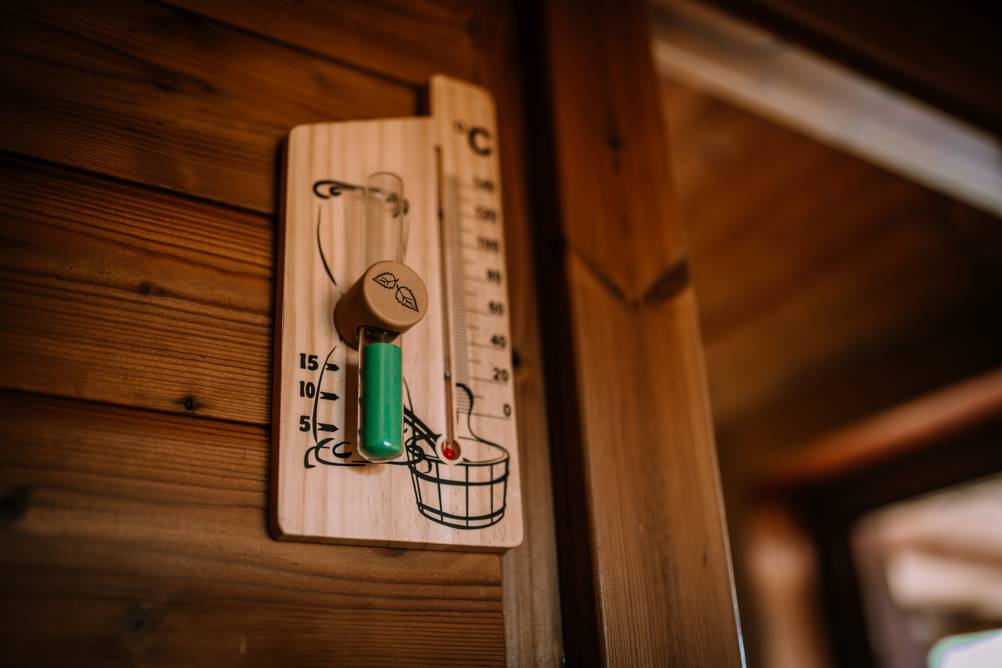 Sauna-Sanduhr im Test: Ein Kombigerät aus Sanduhr und Thermometer ist auf einem hölzernen Träger aufgebracht und an einer Holzwand angebracht.