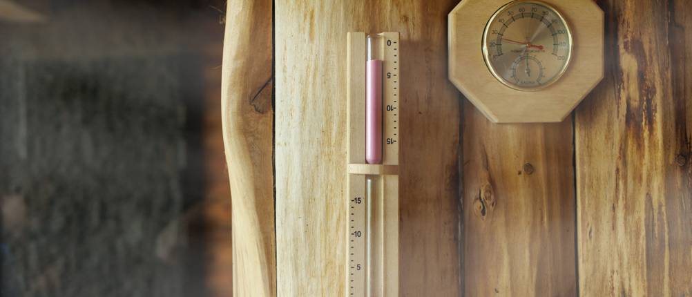 Sauna-Sanduhr im Test: Wand einer rustikalen Holzsauna mit Sanduhr und Hygrometer.
