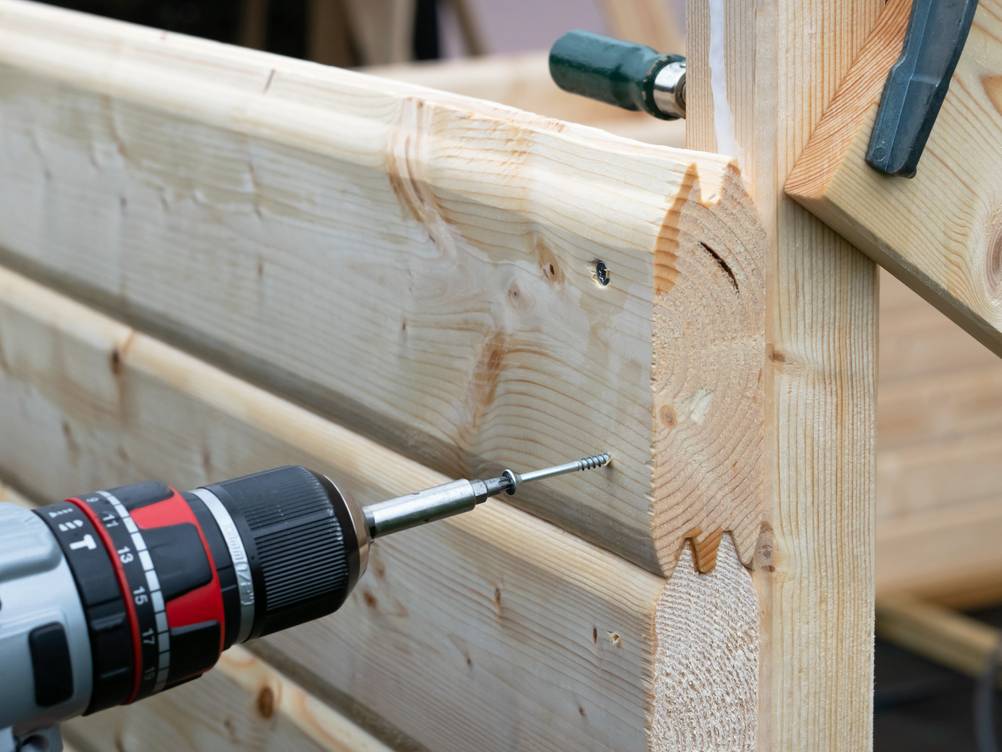 Saunahaus im Test: Eine Schrauber setzt gerade eine Schraube in einer Holzbohle die mit Nut und Federn eine Wand bildet.