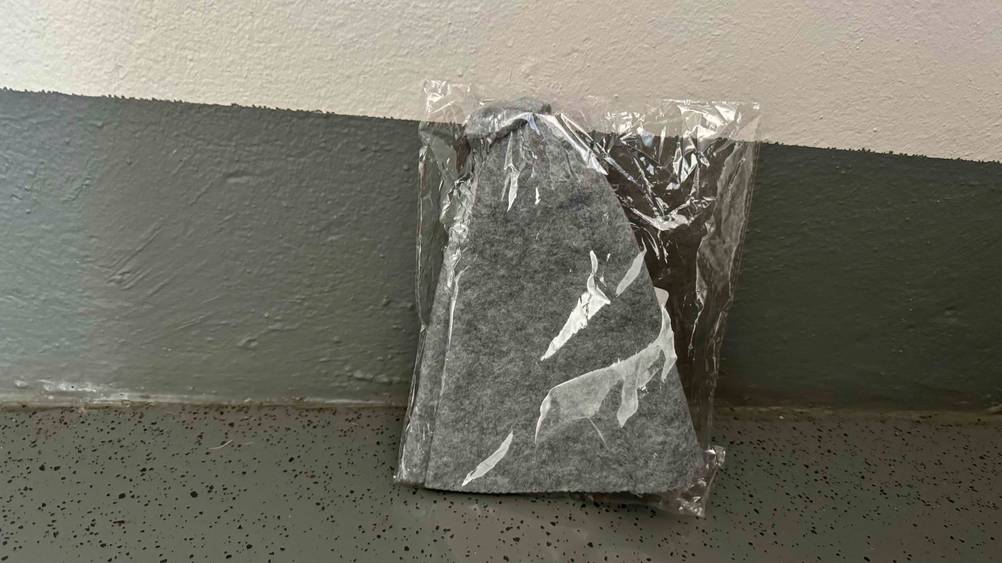 Ein getesteter Saunahut in transparenter Verpackung an einer gestreiften Wand.