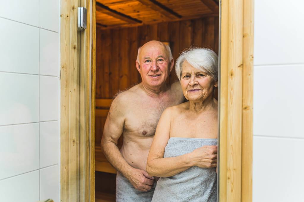 Saunakilt-Damen im Test: Ein älteres Paar steht im Eingang einer Sauna, gehüllt in graues Frottee.