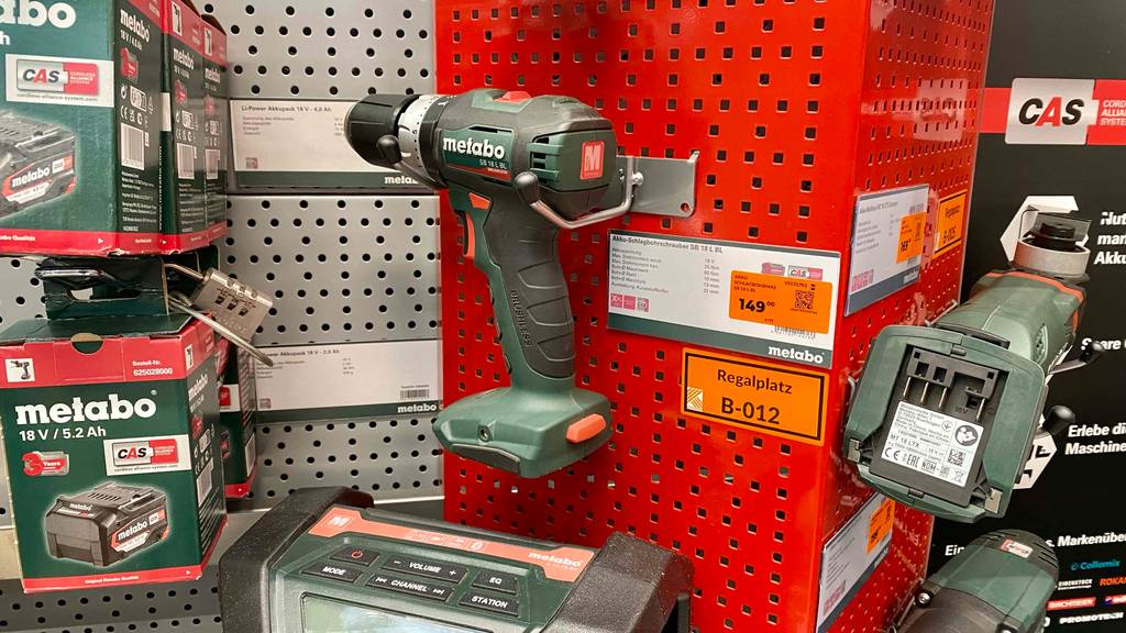 Ein schwarz-grüner Metabo-Akkuschrauber im Test hängt an einer roten Ausstellungswand im Geschäft neben weiteren Produkten der Marke Metabo.
