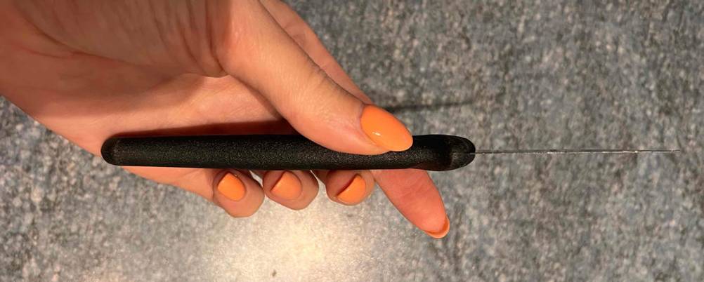 Schälmesser-Test: Hand hält Messer am schwarzen Griff, mit Fokus auf die Schneideklinge vor grauem Hintergrund.