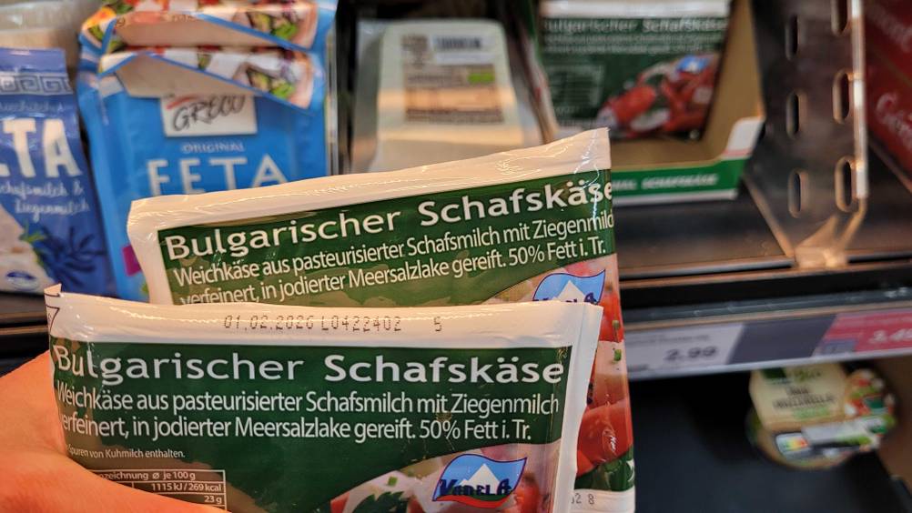 Eine Hand hält zwei Packungen des Schafskäses im Test vor ein Regal.