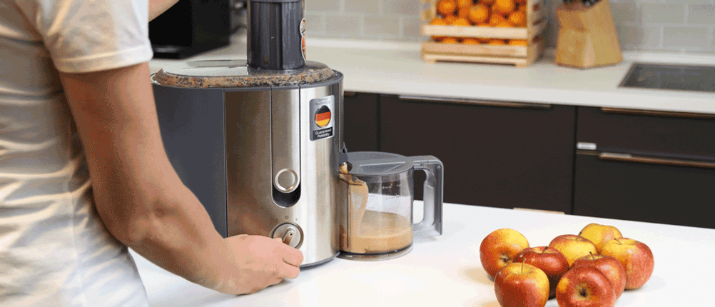 Ein Entsafter steht auf einem Tisch, daneben liegen Äpfel.