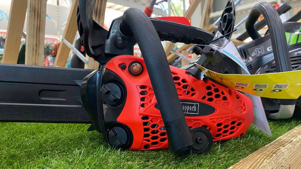 Benzin-Kettensäge im Test: Scheppach-Benzin-Kettensäge mit roter Gehäuseverkleidung steht in einem Ausstellungsbereich.