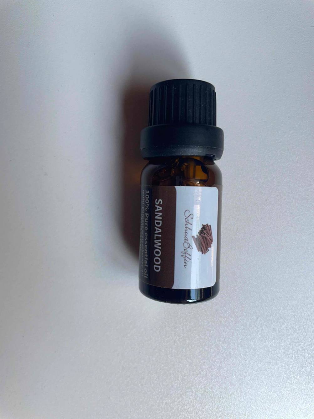 Eine Flasche der getesteten ätherischen Öle mit Duftrichtung Sandelholz liegt auf einer hellen Fläche.