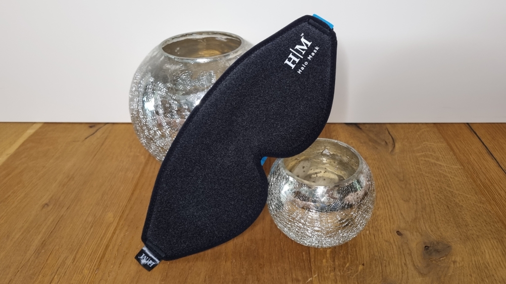 Schlafmaske Marke HM Halo Mask liegt auf zwei Kerzen zur Abbildung.