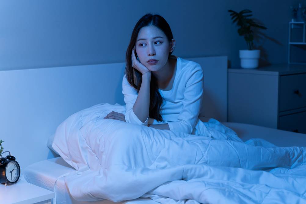 Eine Frau sitzt wach in ihrem Bett und kann nicht schlafen. Sie stütz ihren Kopf auf einer Hand ab.