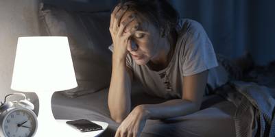 Eine Frau liegt im Bett und fasst sich verzweufelt an den Kopf.