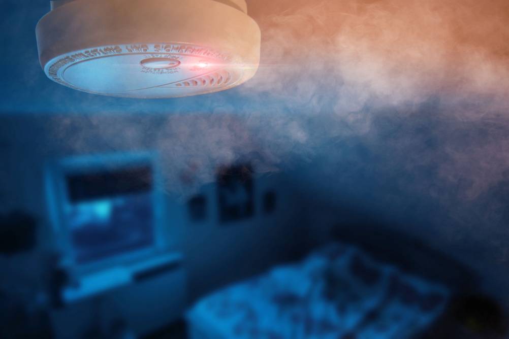 In einem dunklen Schlafzimmer in der Nacht reagiert ein Rauchmelder auf Rauch.