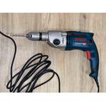 Eine Bosch-Professional-GSB 21-2 RCT-Schlagbohrmaschine mit eingespanntem Betonbohrer liegt auf hellem Holzuntergrund.