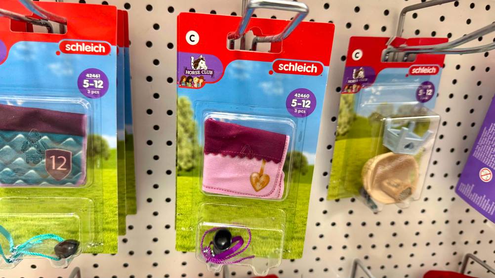 Verschiedene Packungen des getesteten Schleich-Pferde-Zubehörs hängen in einem Regal.