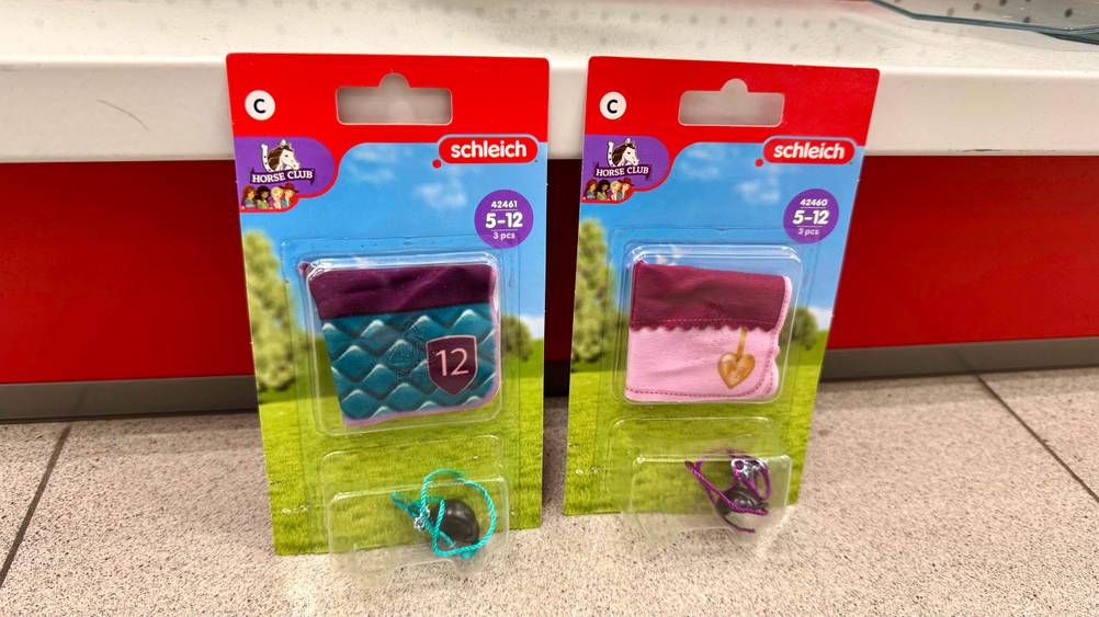 Schleich-Pferde-Zubehör im Test: Zwei Packungen nebeneinander vor einem roten Regal auf dem Boden.