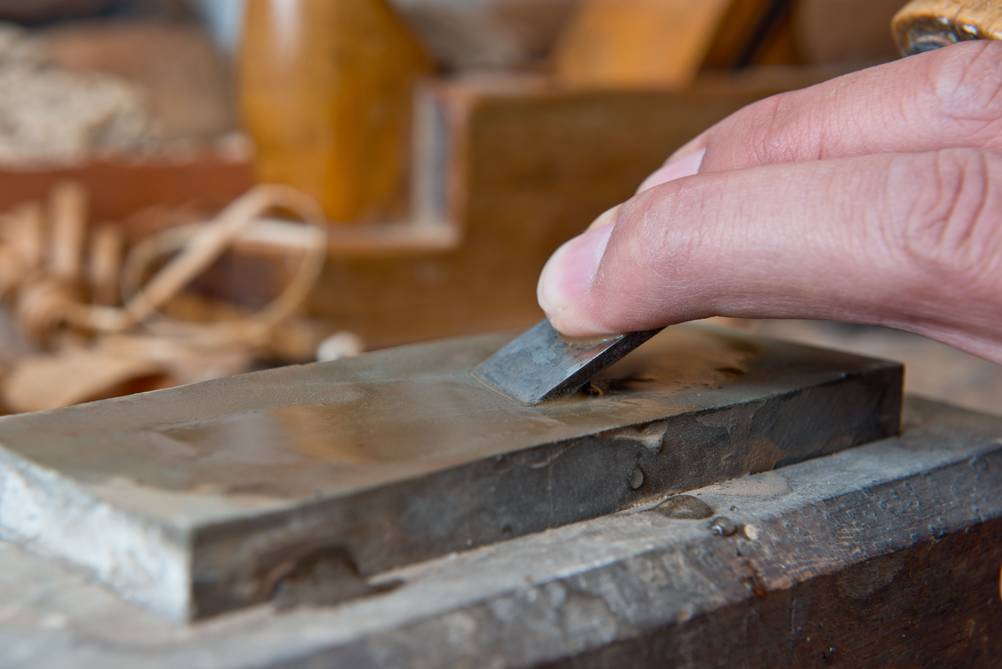 Schleifhilfe-Stechbeitel im Test: Finger führen einen Stechbeitel über einen angefeuchteten Schleifstein.